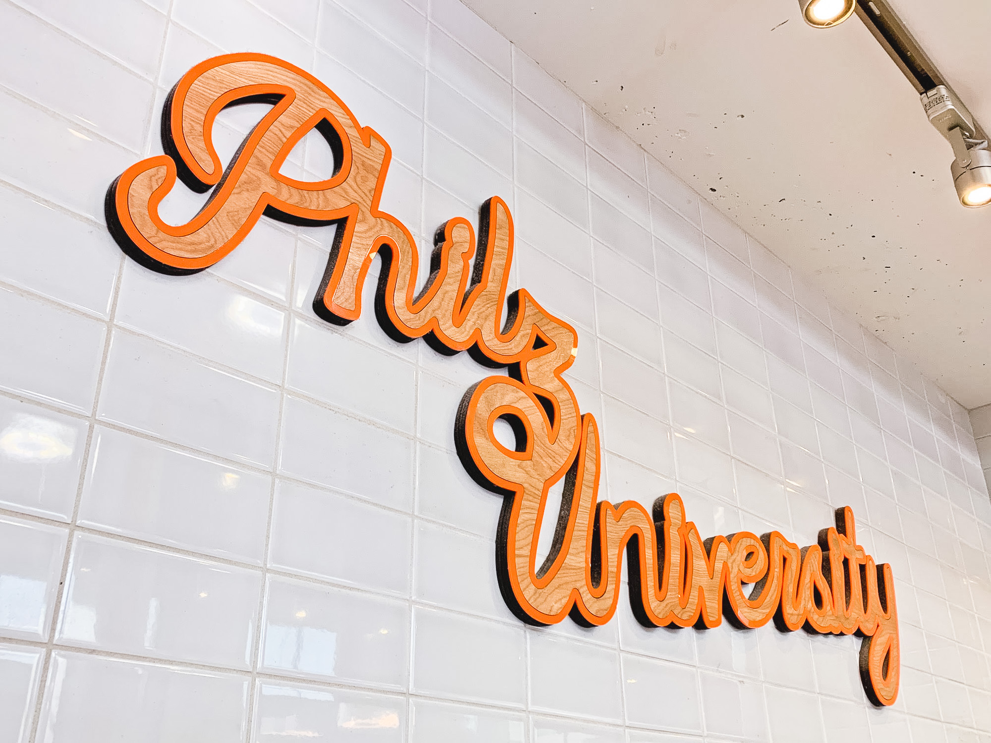 Orange and light wood script sign on white tile wall for Philz University in San Francisco