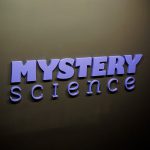 Purple letters on dark grey wall for the Knotel designed Mystery Science lobby, a company that provides open-and-go lessons that inspire kids to love science.