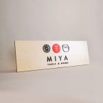 Raised black, red, and light wood sign with icons for Miya Table & Home, a third-generation family owned business, importing Japanese tableware and gifts since 1947.