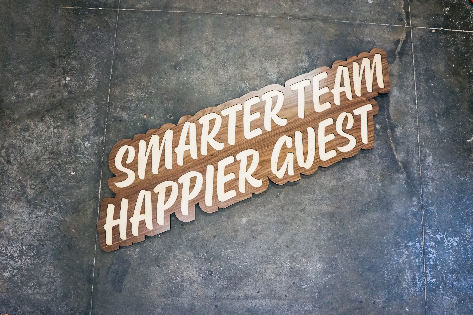 Script wood sign for “Smarter Team, Happier Guest” Quore office. Script wood sign for