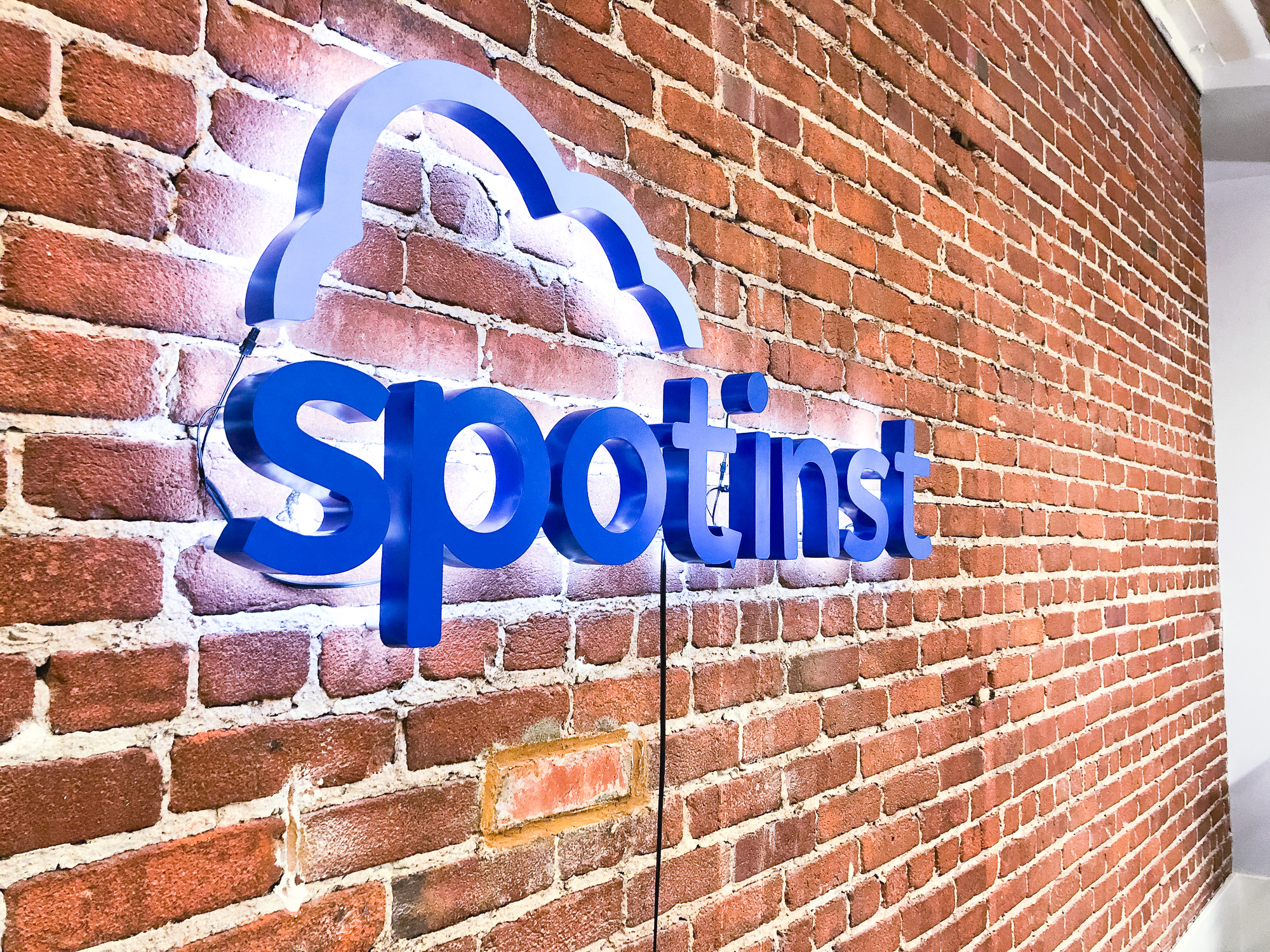 Illuminated, painted blue sign on brick conference room wall for Spotinst, a San Francisco company that creates intelligent workload software.