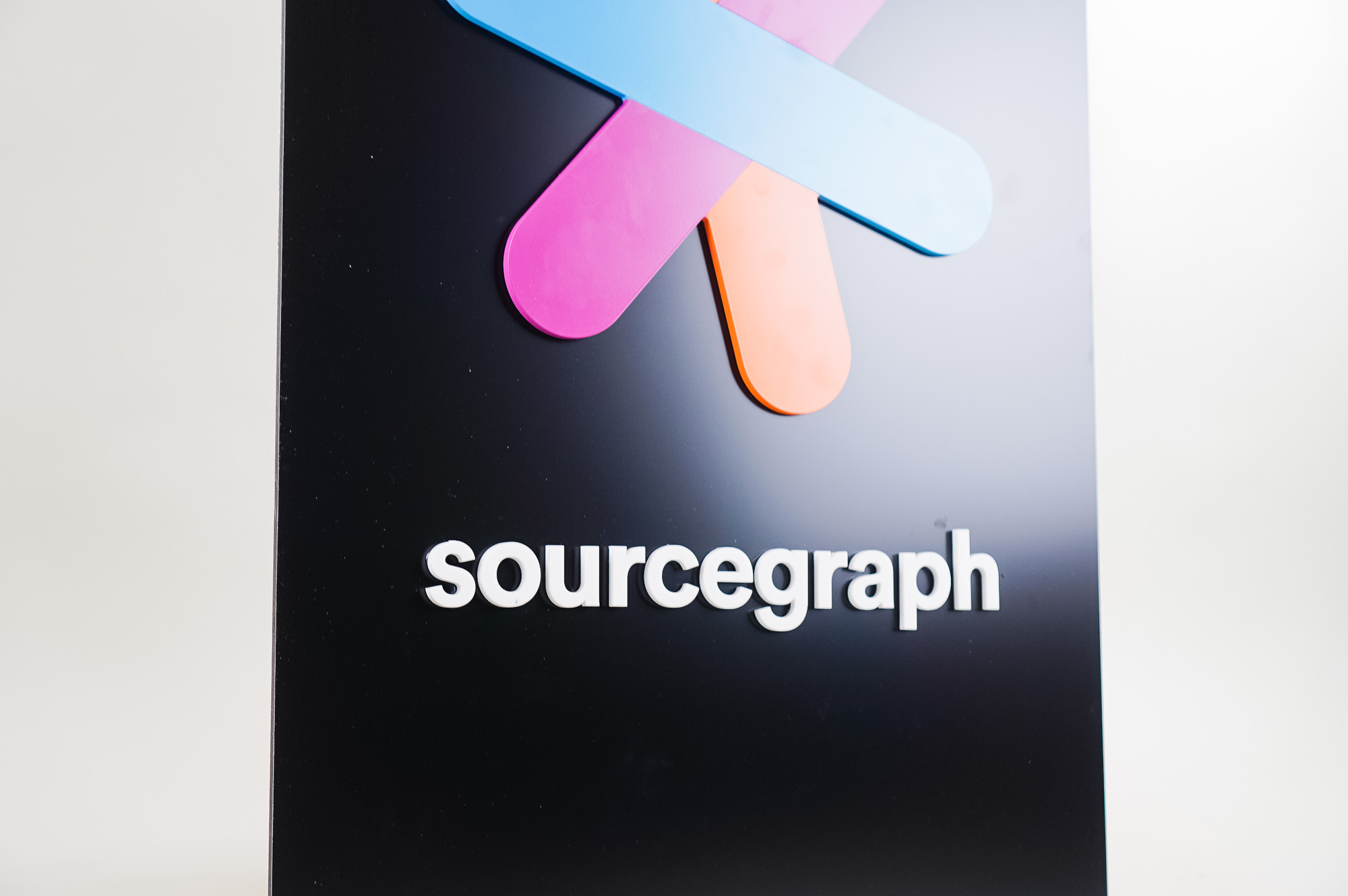 Simple black blade sign with colored logo for Sourcegraph, a San Francisco-based company that adds code intelligence to GitHub and other code hosts.