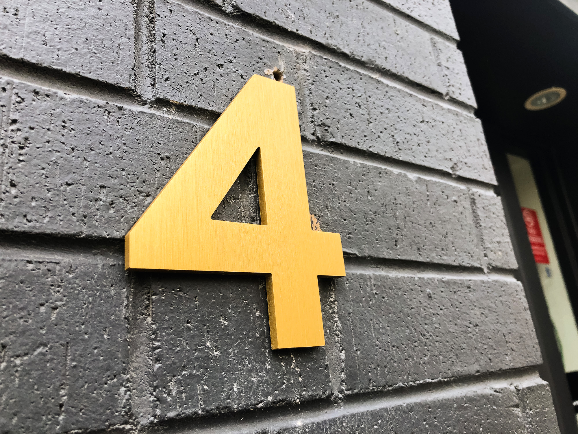anodized brushed gold number on black brick building