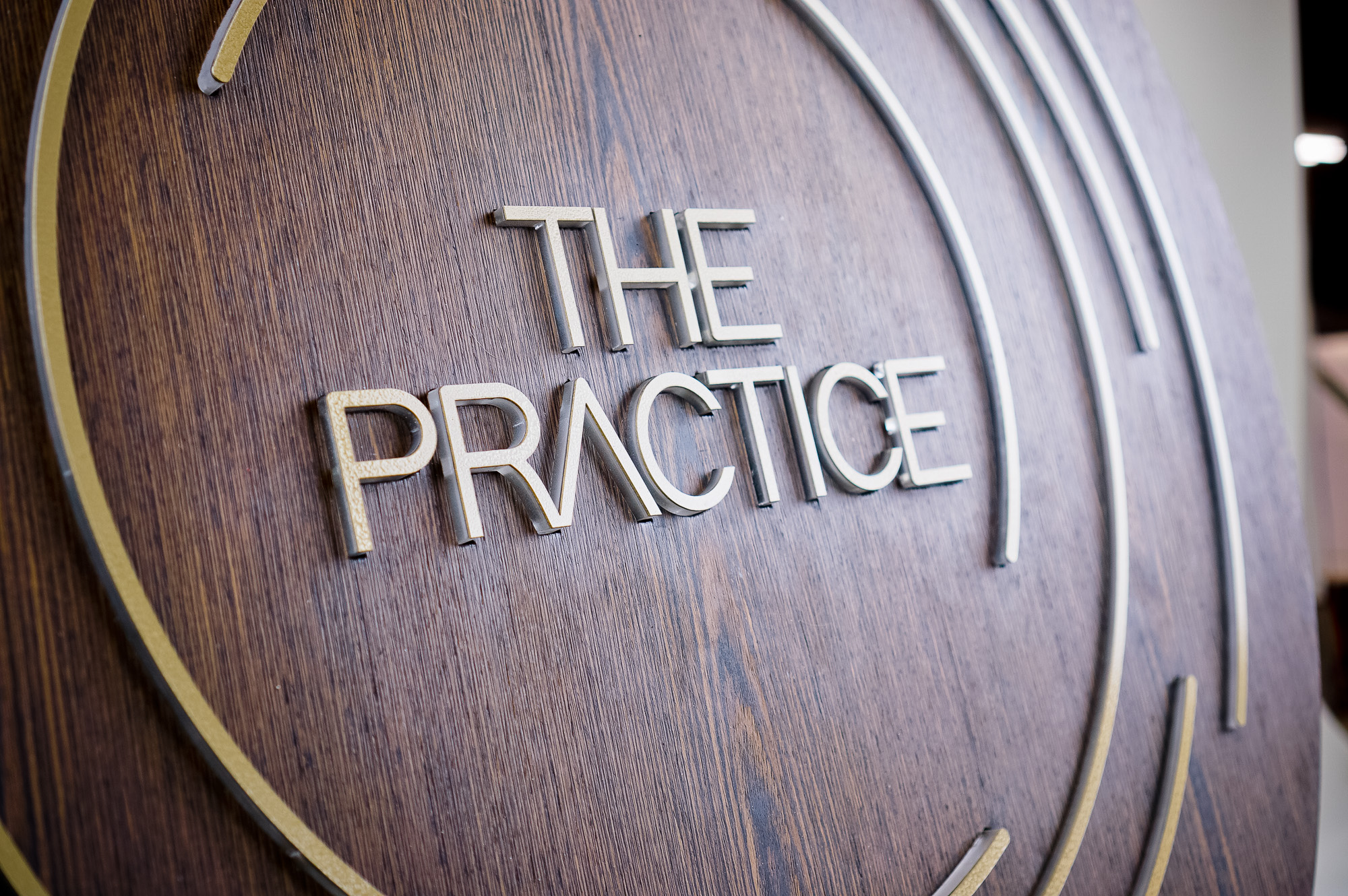 Illuminated dark wood and brass sign for The Practice, a yoga studio at Newtown Athletic Club, a premiere family fitness and wellness center serving residents of Newtown, PA
