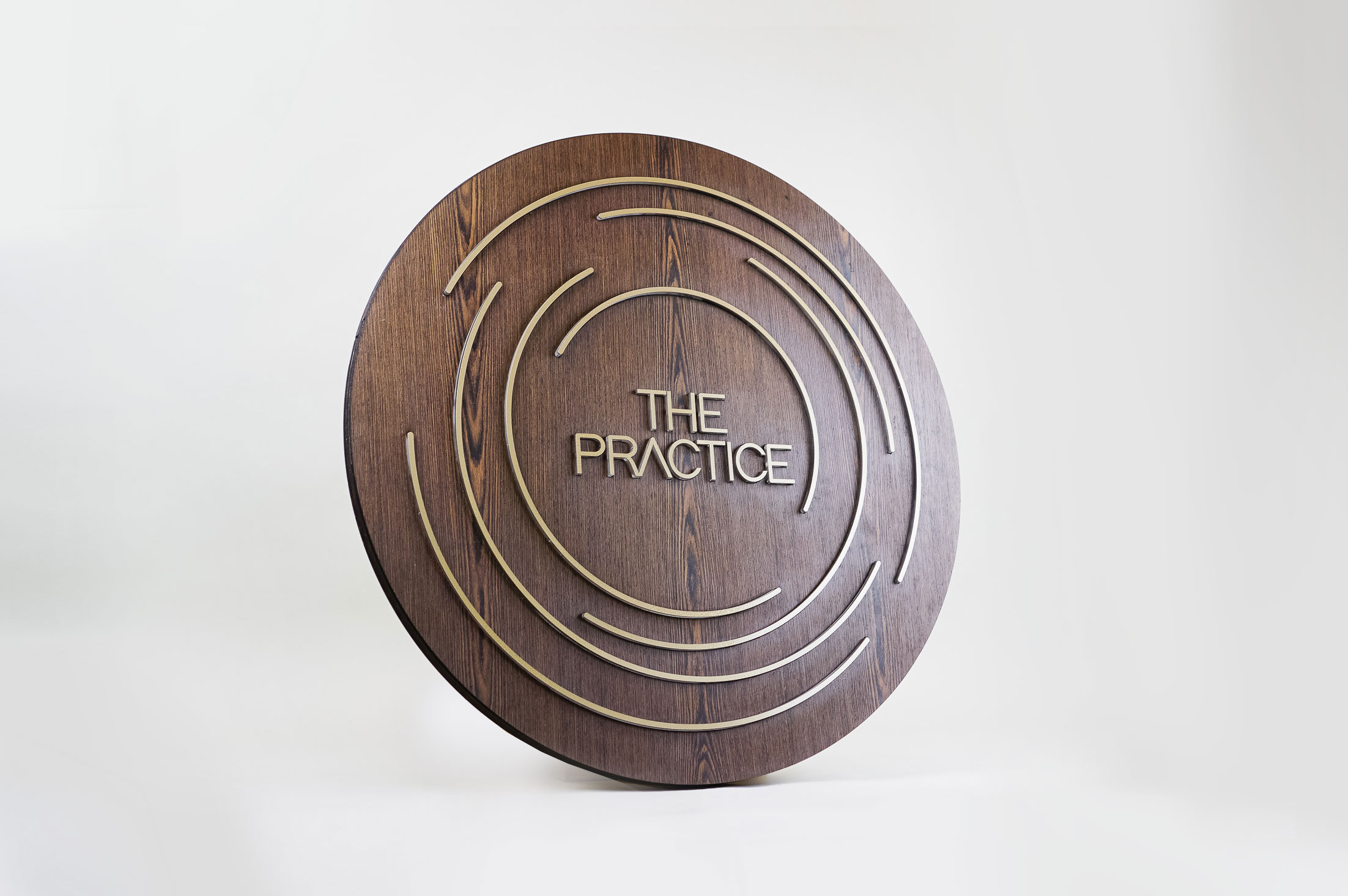Illuminated dark wood and brass sign for The Practice, a yoga studio at Newtown Athletic Club, a premiere family fitness and wellness center serving residents of Newtown, PA Illuminated dark wood and brass sign for The Practice, a yoga studio at Newtown Athletic Club, a premiere family fitness and wellness center serving residents of Newtown, PA