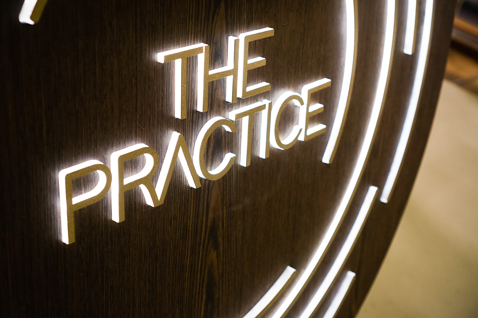 Illuminated dark wood and brass sign for The Practice, a yoga studio at Newtown Athletic Club, a premiere family fitness and wellness center serving residents of Newtown, PA Illuminated dark wood and brass sign for The Practice, a yoga studio at Newtown Athletic Club, a premiere family fitness and wellness center serving residents of Newtown, PA