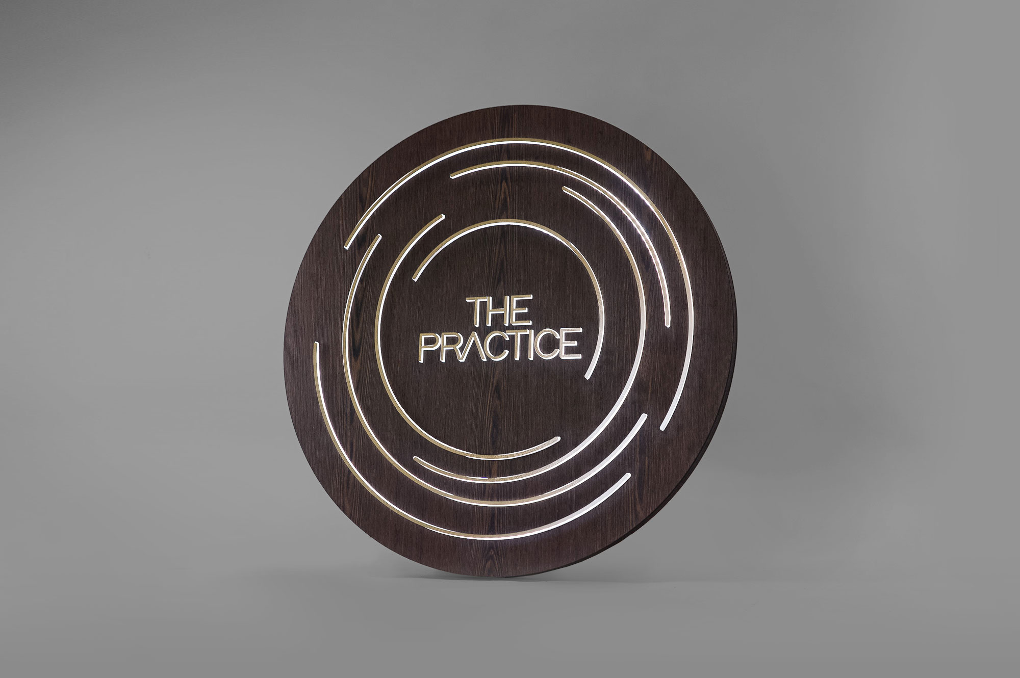 Illuminated dark wood and brass sign for The Practice, a yoga studio at Newtown Athletic Club, a premiere family fitness and wellness center serving residents of Newtown, PA