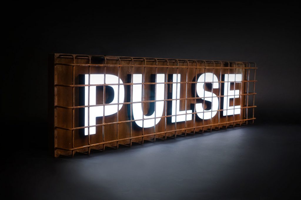 Industrial, caged, rusty metal illuminated sign for Pulse, a fitness studio at Newtown Athletic Club, a premiere family fitness and wellness center serving residents of Newtown, PA