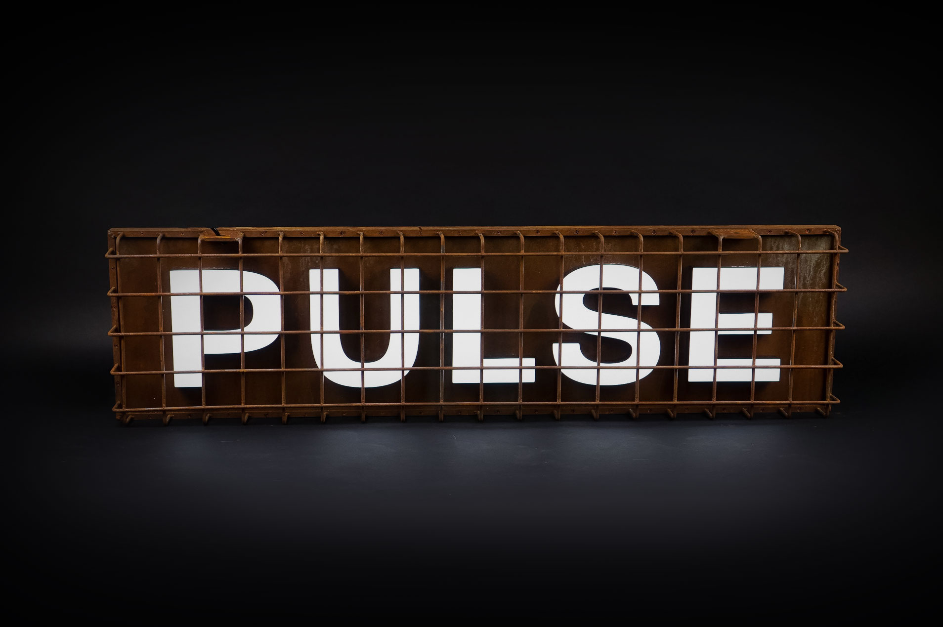 Industrial, caged, rusty metal illuminated sign for Pulse, a fitness studio at Newtown Athletic Club, a premiere family fitness and wellness center serving residents of Newtown, PA Industrial, caged, rusty metal illuminated sign for Pulse, a fitness studio at Newtown Athletic Club, a premiere family fitness and wellness center serving residents of Newtown, PA