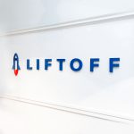 Rocket logo sign on white wall for Liftoff, a company that creates a mobile app optimization marketing platform. Office designed by Knotel, an office space rental agency.