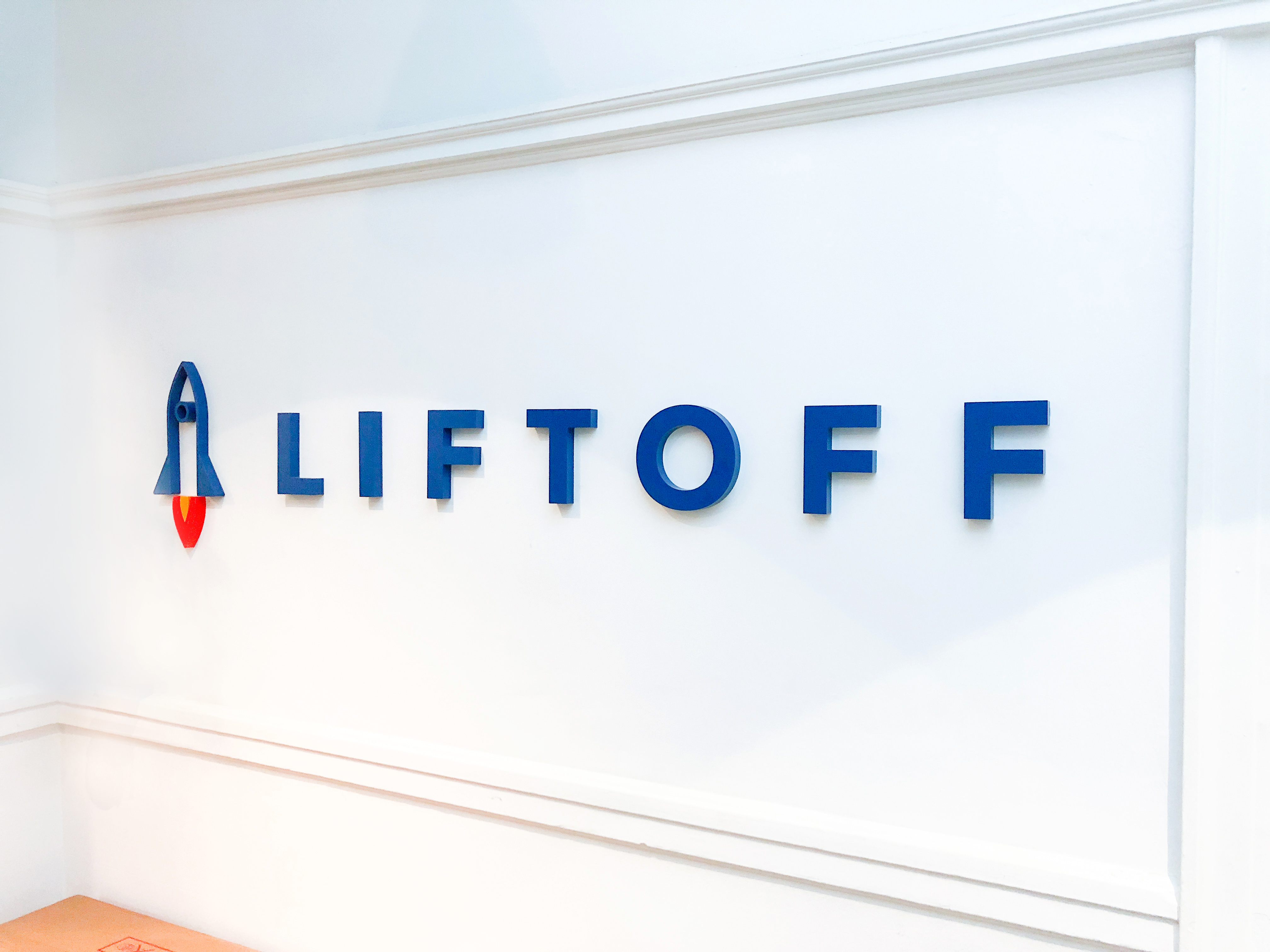 Rocket logo sign on white wall for Liftoff, a company that creates a mobile app optimization marketing platform. Office designed by Knotel, an office space rental agency.