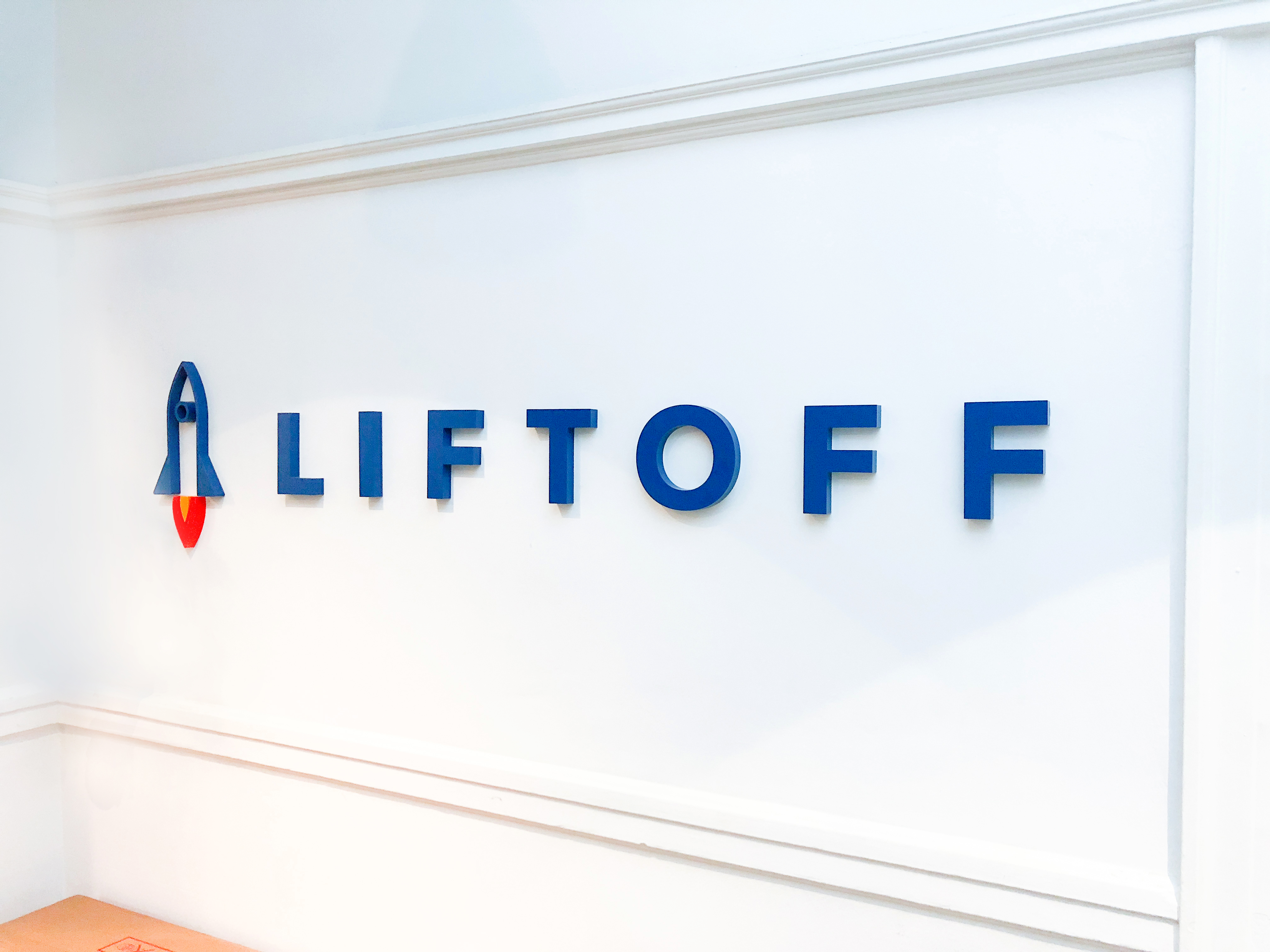 Rocket logo sign on white wall for Liftoff, a company that creates a mobile app optimization marketing platform. Office designed by Knotel, an office space rental agency. Rocket logo sign on white wall for Liftoff, a company that creates a mobile app optimization marketing platform. Office designed by Knotel, an office space rental agency.