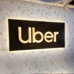 Illuminated black wood lobby sign with warm light on geometrical wallpaper for Uber, an American multinational transportation network company..