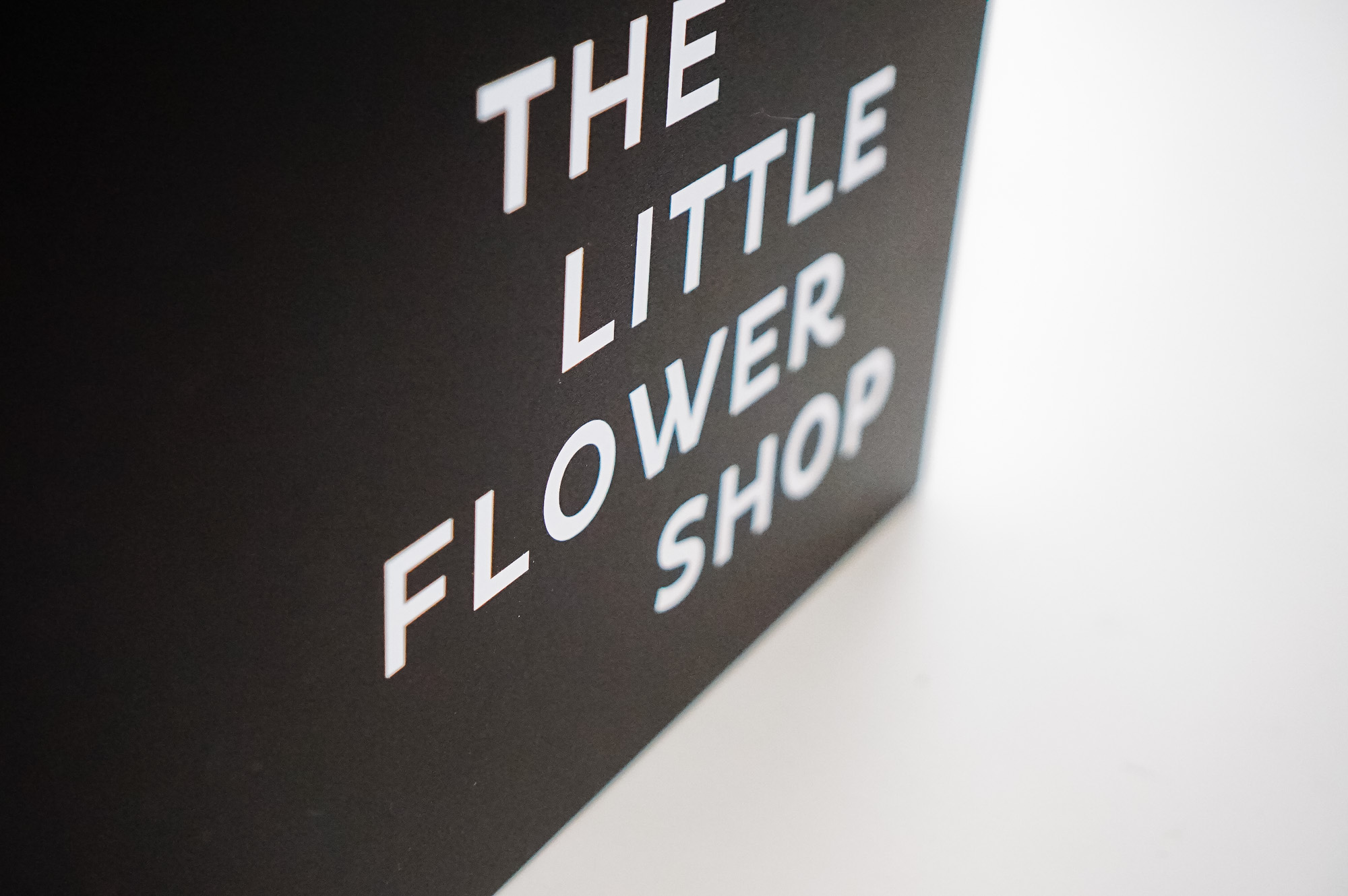 Modern, narrow, banner-like black and white blade sign for The Little Flower Shop, a florist in Larkspur, CA. Modern, narrow, banner-like black and white blade sign for The Little Flower Shop, a florist in Larkspur, CA.