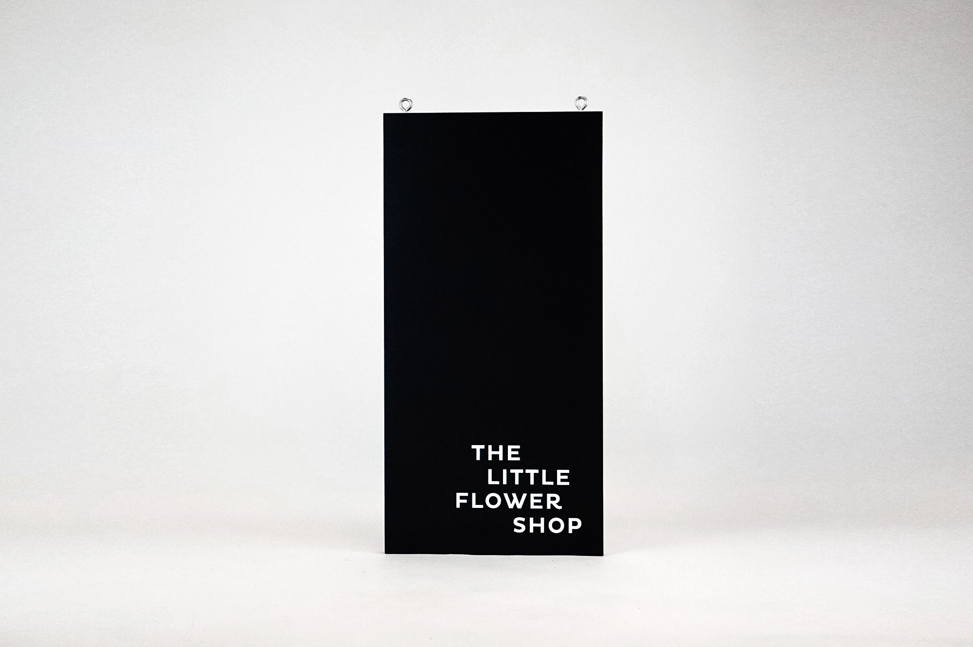 Modern, narrow, banner-like black and white blade sign for The Little Flower Shop, a florist in Larkspur, CA. Modern, narrow, banner-like black and white blade sign for The Little Flower Shop, a florist in Larkspur, CA.