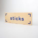 Light wood event sign with blue logo for Sticks, a kidswear company.