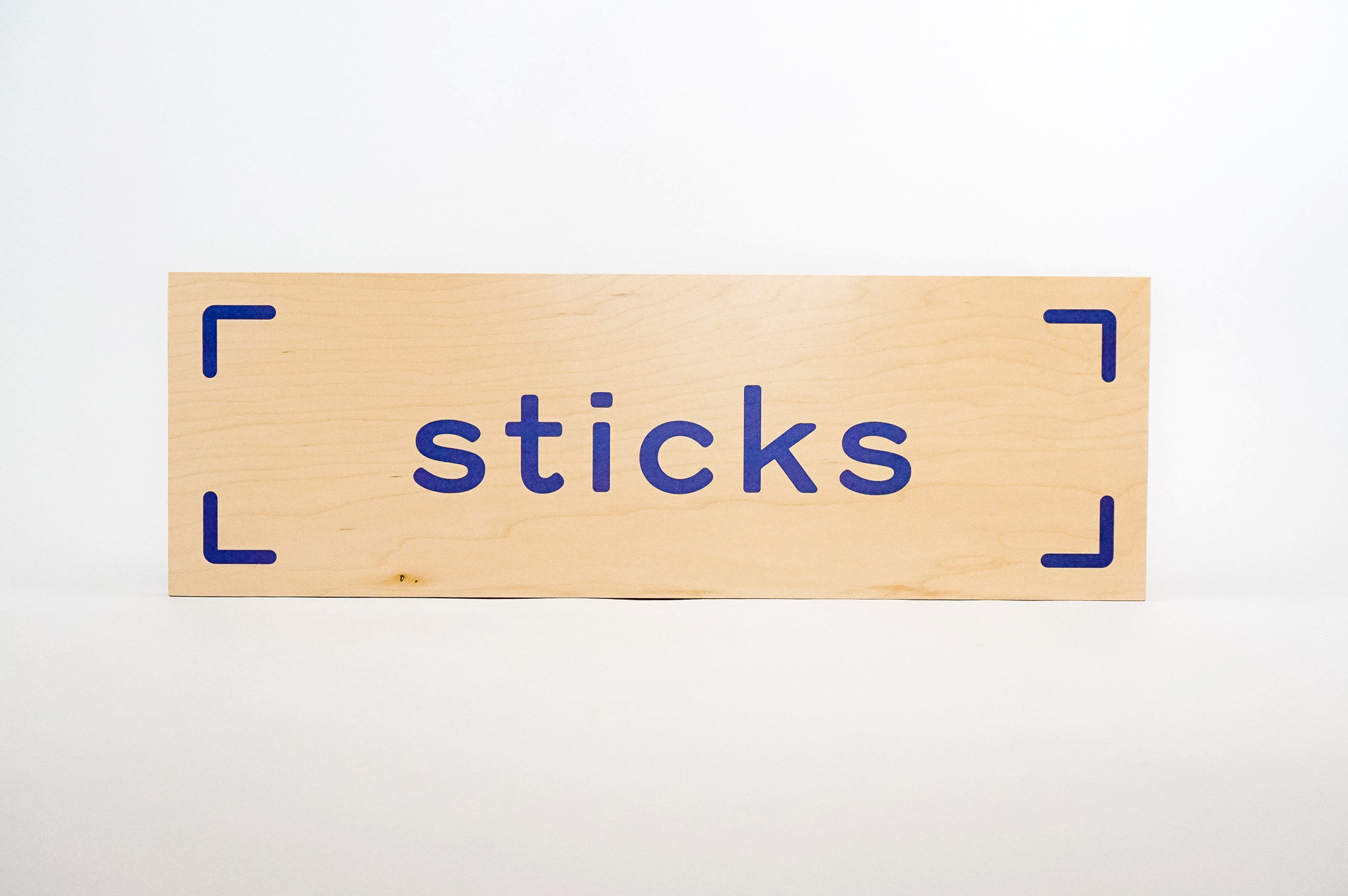 Light wood event sign with blue logo for Sticks, a kidswear company.