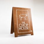 Dark wood sidewalk A-frame sign with white logo for The Chop House, a bar and lounge in Toledo, Ohio.