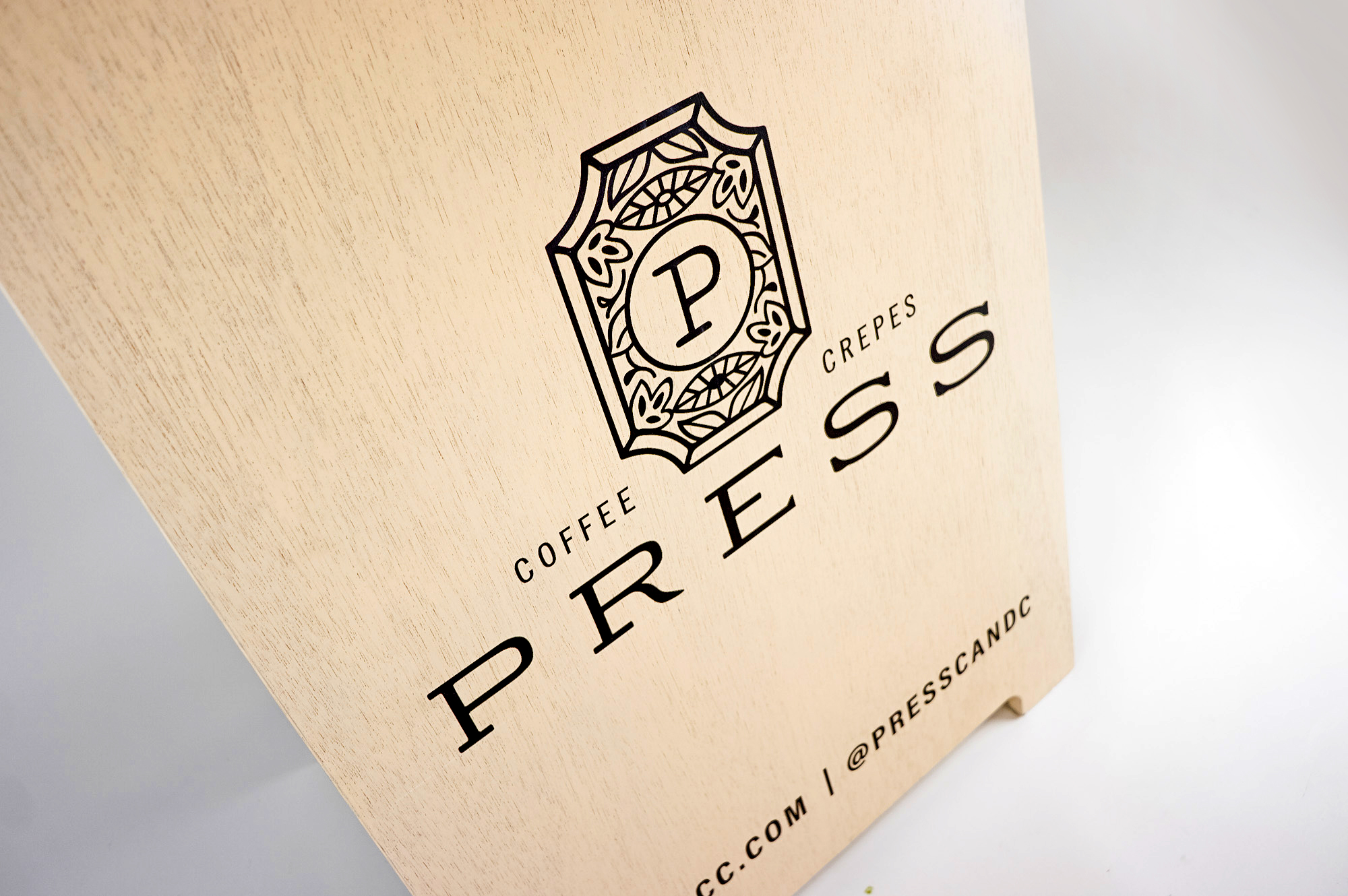 Light wood A-frame sidewalk sign with intricate black logo and text for Press, a European-Inspired coffeehouse and crêperie in downtown Graham, NC. Light wood A-frame sidewalk sign with intricate black logo and text for Press, a European-Inspired coffeehouse and crêperie in downtown Graham, NC.