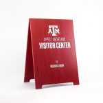 Red A-frame sign with white text for the visitor center at Texas A&M, a public research university in College Station, Texas.