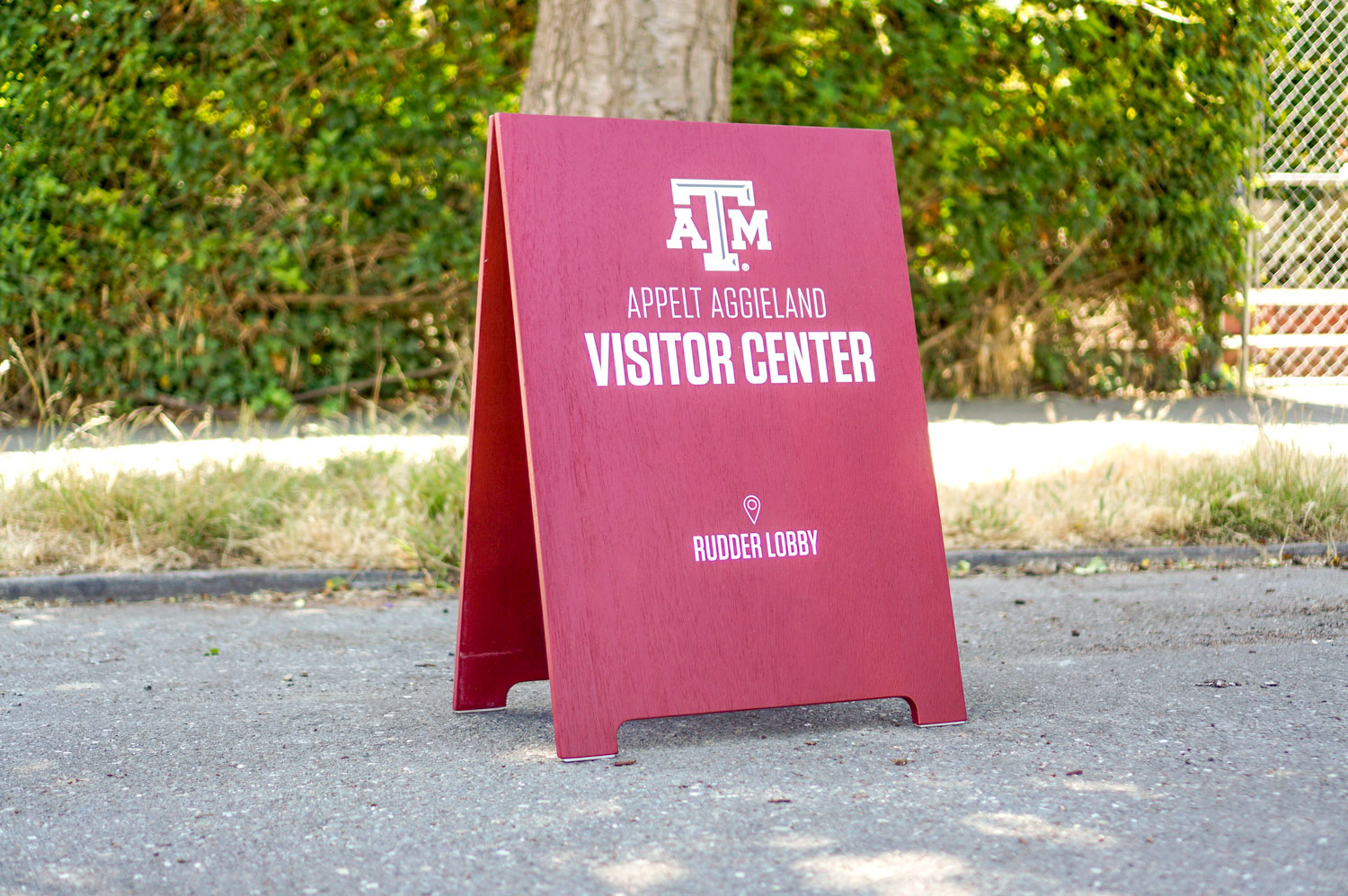 Red A-frame sign with white text for the visitor center at Texas A&M, a public research university in College Station, Texas. Red A-frame sign with white text for the visitor center at Texas A&M, a public research university in College Station, Texas.