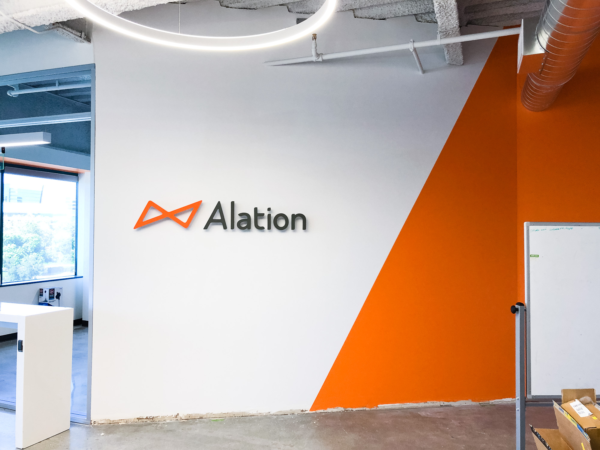 Illuminated black and orange lobby sign on color blocked wall for Alation, a data catalog company based in Redwood City, CA