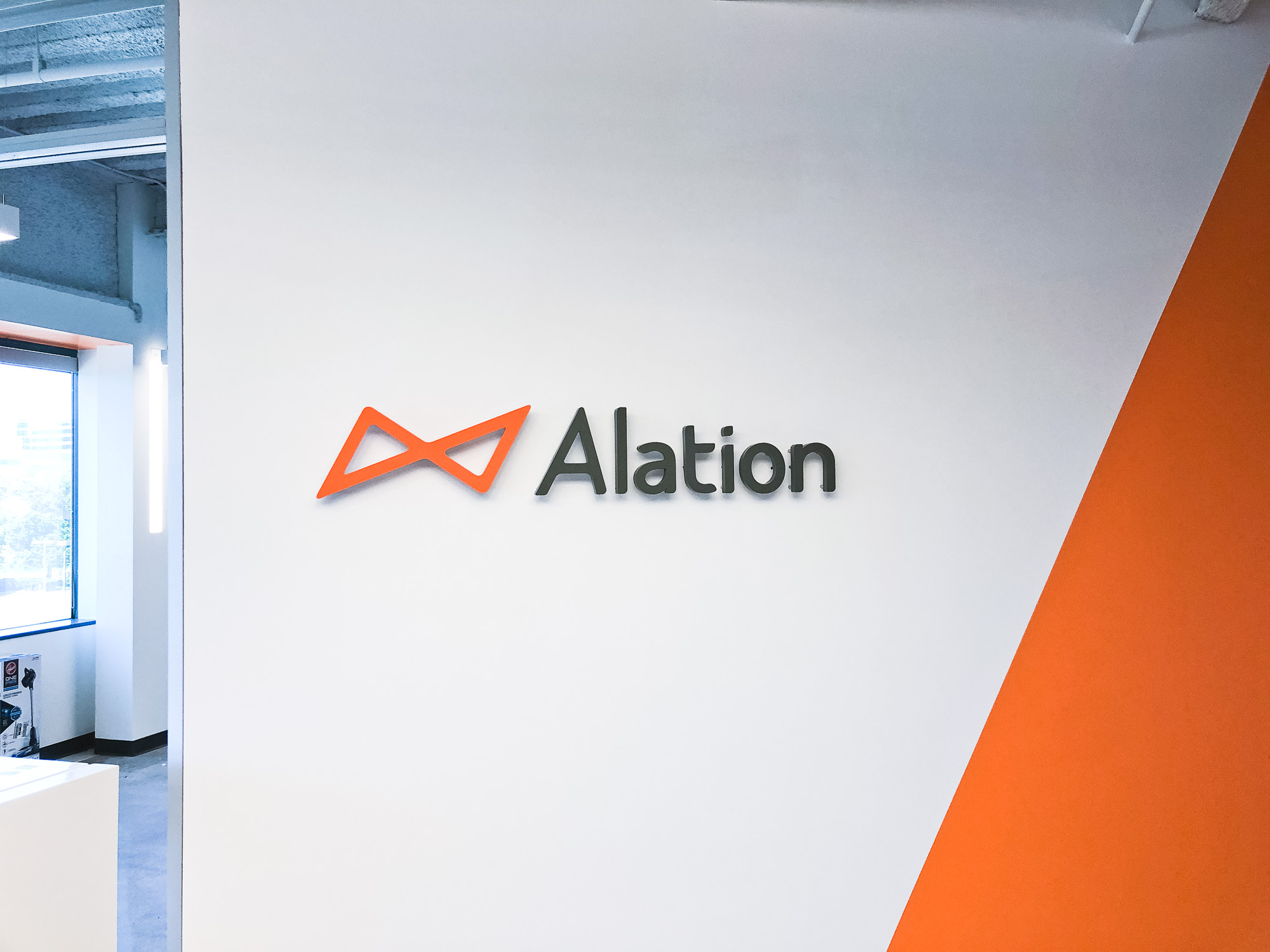 Illuminated black and orange lobby sign on color blocked wall for Alation, a data catalog company based in Redwood City, CA