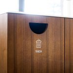 Minimal white vinyl signage /decals for wood trash, compost, and recycling bins at the office of Baker McKenzie, a multinational law firm.