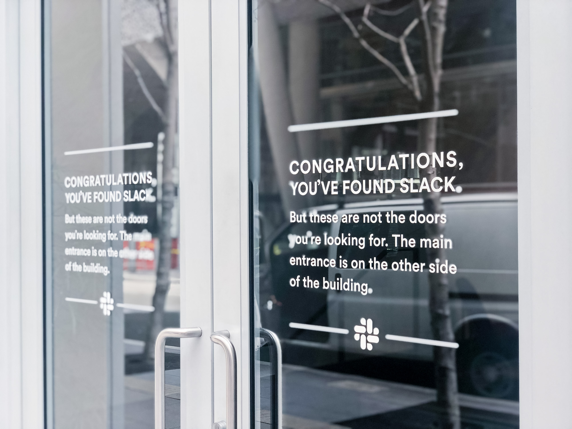 Matte white vinyl wayfinding sign with white text on glass doors for the San Francisco office of Slack, an American cloud-based set of proprietary team collaboration tools and services. Matte white vinyl wayfinding sign with white text on glass doors for the San Francisco office of Slack, an American cloud-based set of proprietary team collaboration tools and services.