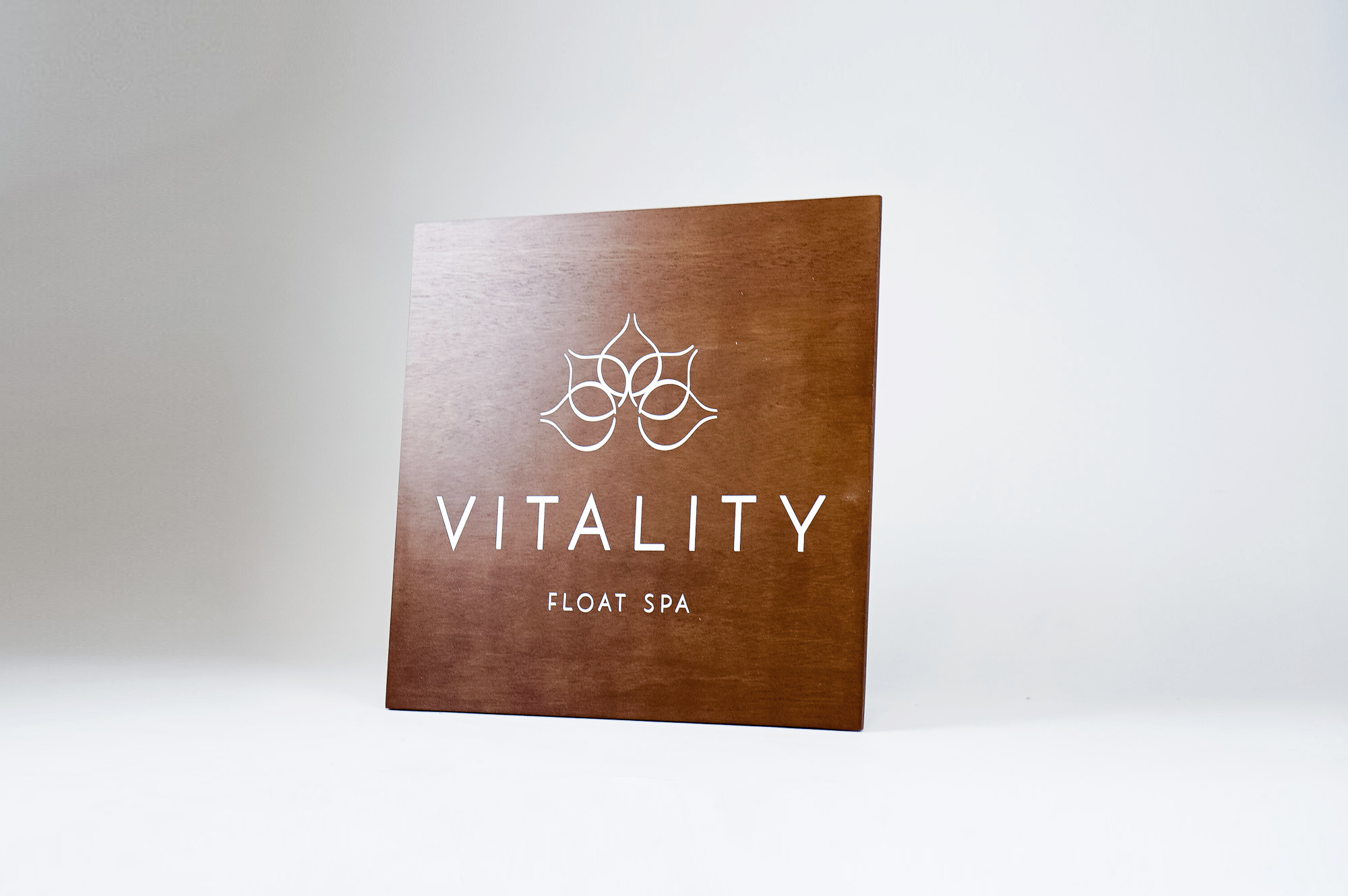 Dark wood retail blade sign with white artwork for Vitality, a massage therapy and wellness studio located in Carytown, Virginia. Dark wood retail blade sign with white artwork for Vitality, a massage therapy and wellness studio located in Carytown, Virginia.