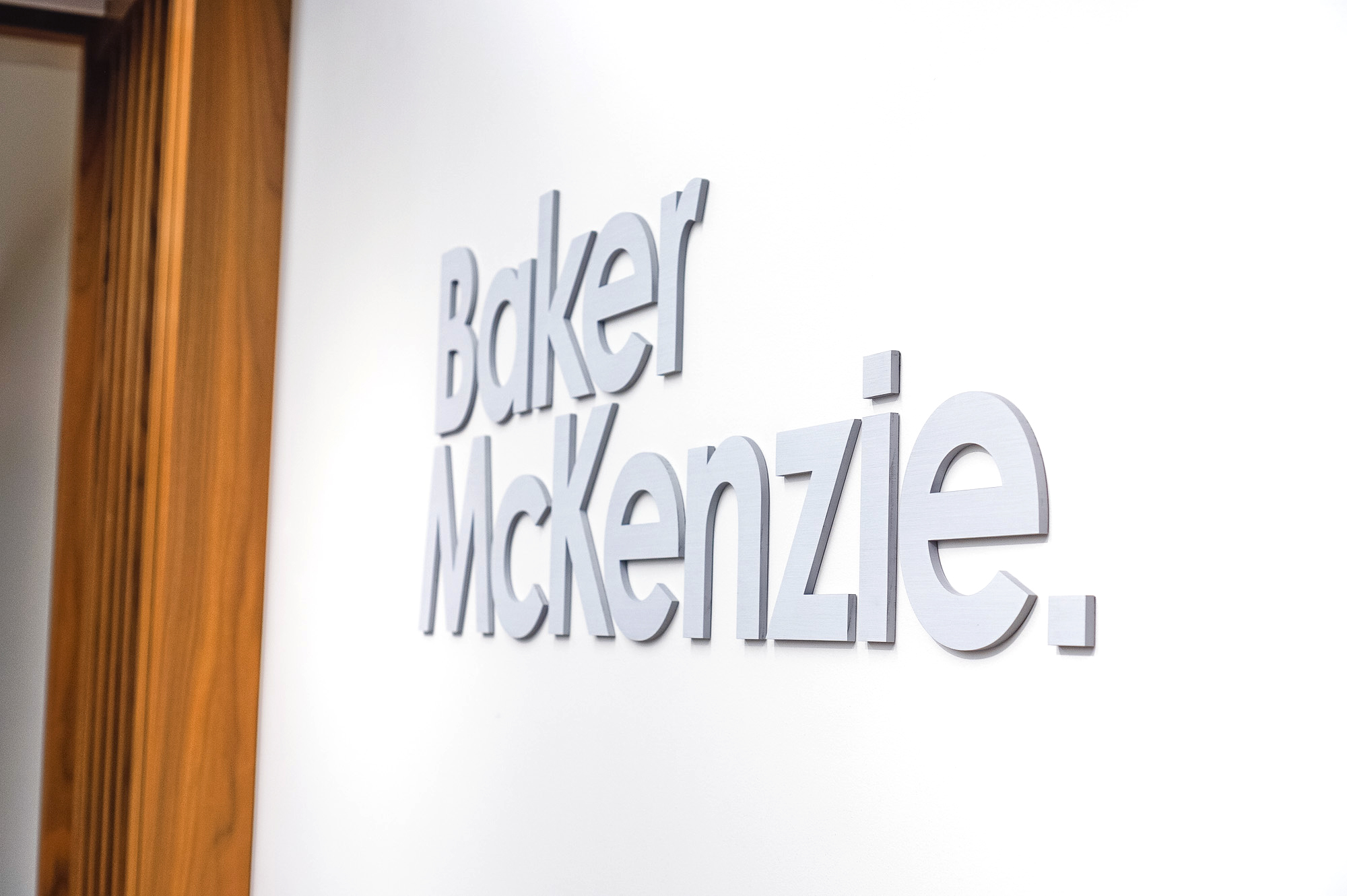 Brushed metal lobby sign on white wall at the office of Baker McKenzie, a multinational law firm.