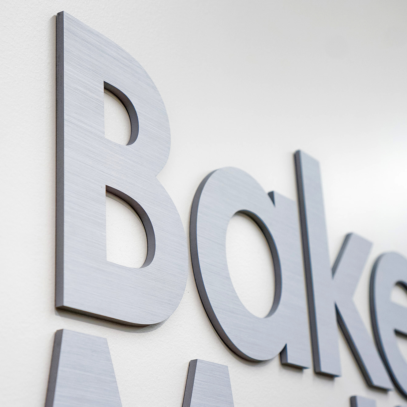 Brushed metal lobby sign on white wall at the office of Baker McKenzie, a multinational law firm. Brushed metal lobby sign on white wall at the office of Baker McKenzie, a multinational law firm.