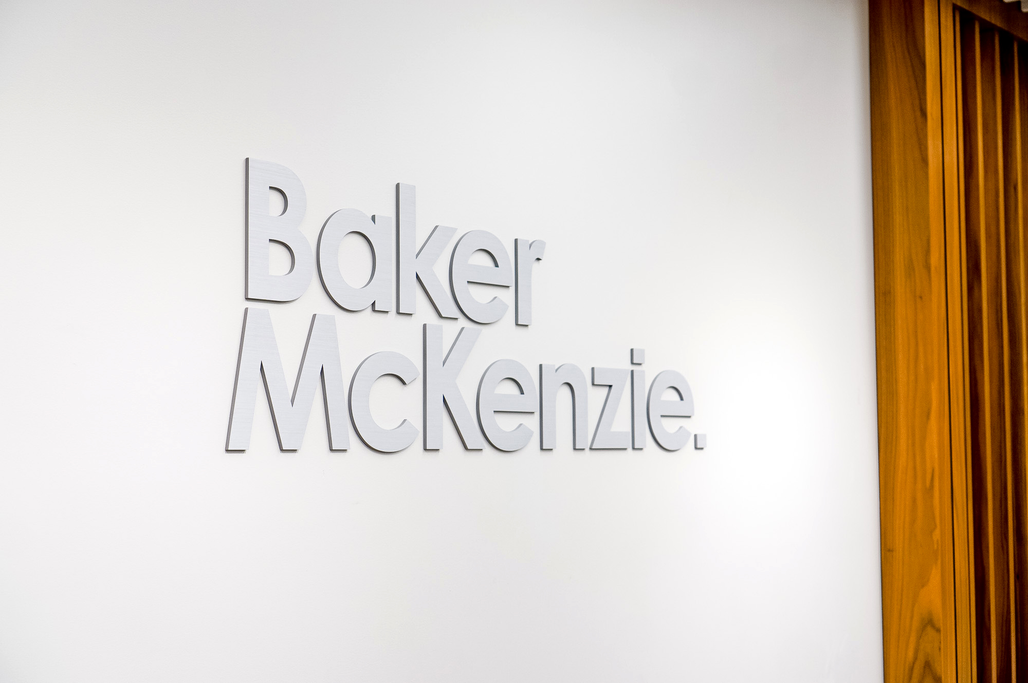 Brushed metal lobby sign on white wall at the office of Baker McKenzie, a multinational law firm. Brushed metal lobby sign on white wall at the office of Baker McKenzie, a multinational law firm.
