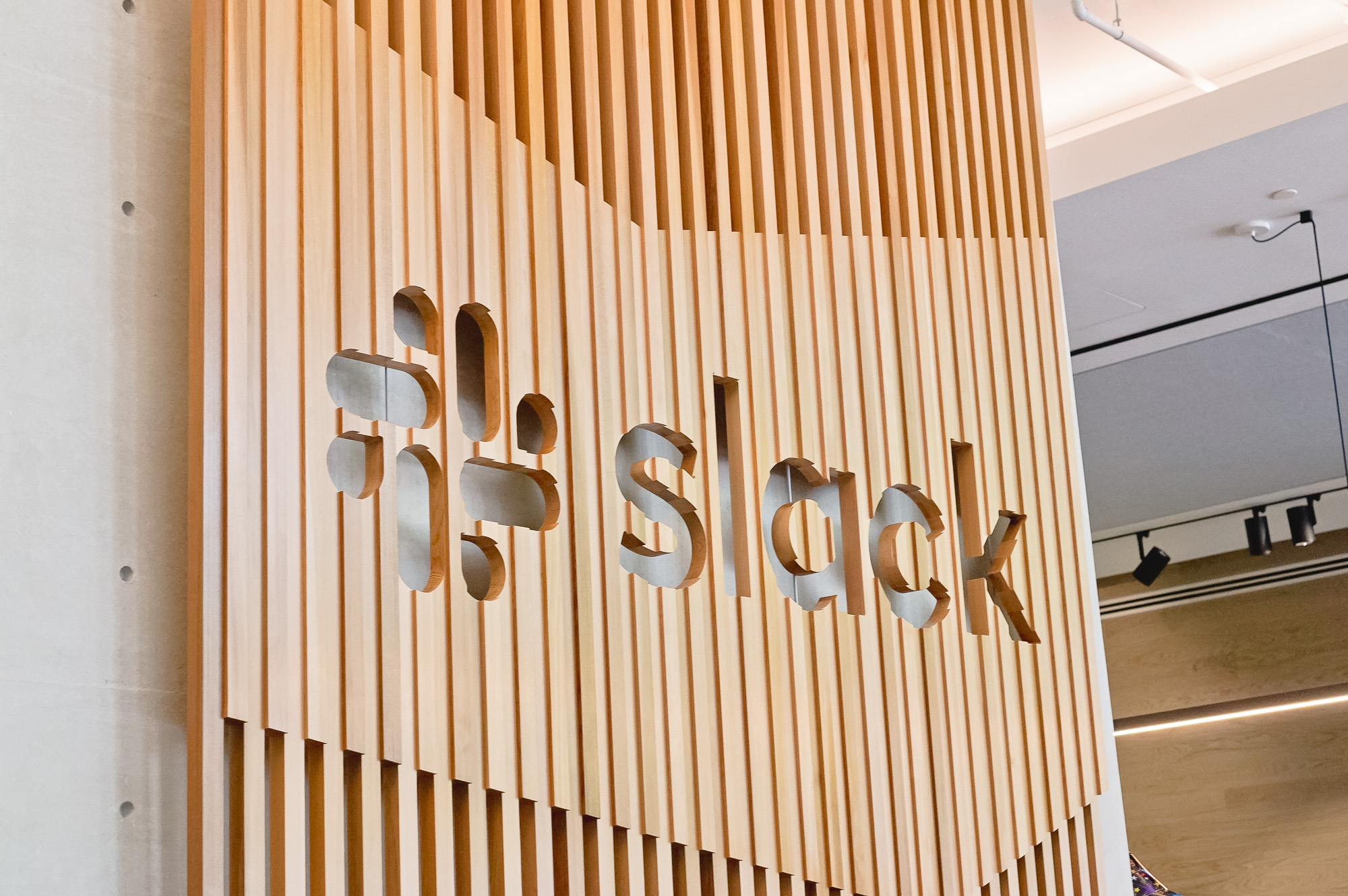 Modern, large-scale slat wood lobby sign on concrete wall at the San Francisco lobby of Slack, an American cloud-based set of team collaboration tools and services.