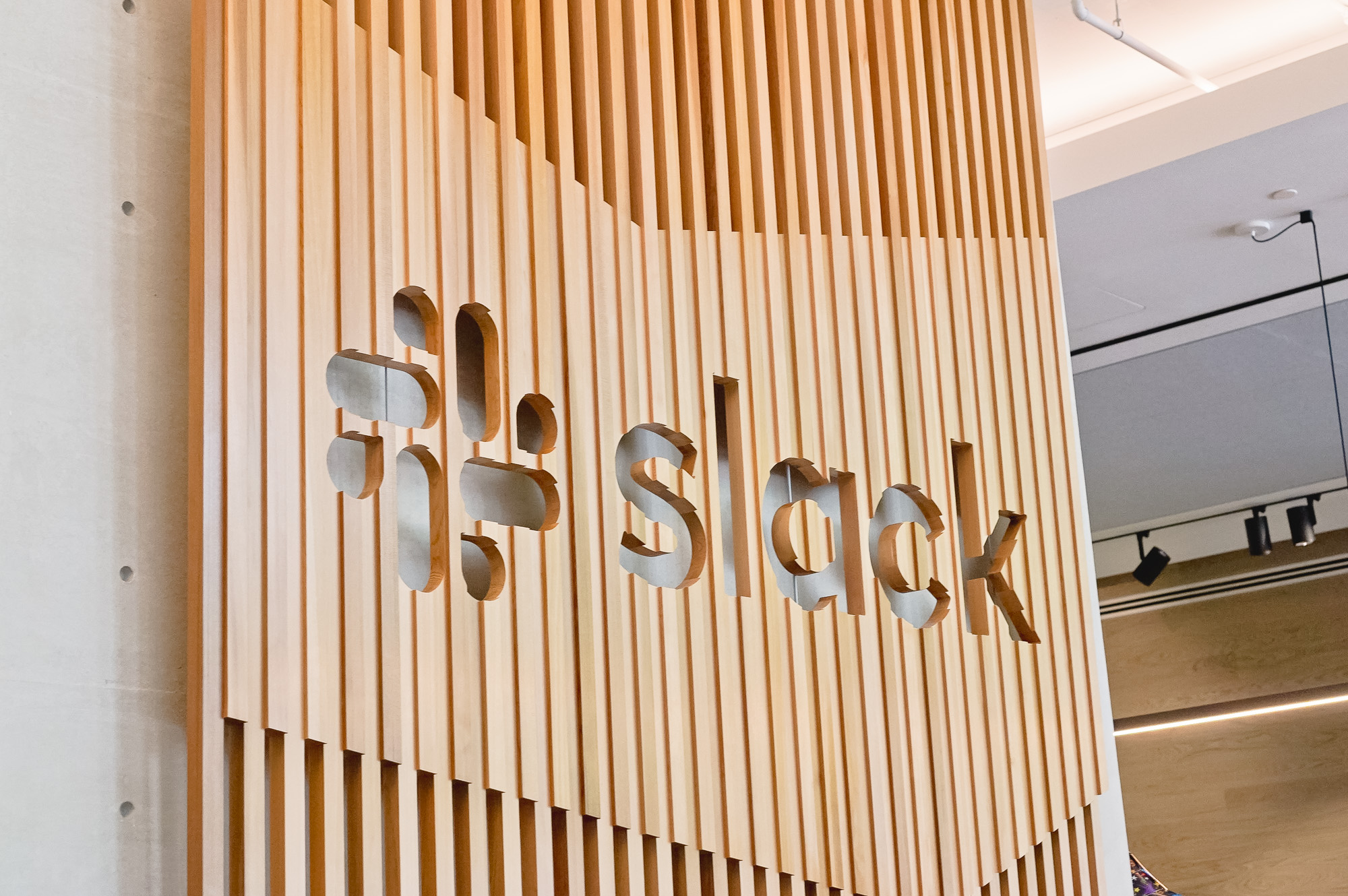 Modern, large-scale slat wood lobby sign on concrete wall at the San Francisco lobby of Slack, an American cloud-based set of team collaboration tools and services. Modern, large-scale slat wood lobby sign on concrete wall at the San Francisco lobby of Slack, an American cloud-based set of team collaboration tools and services.