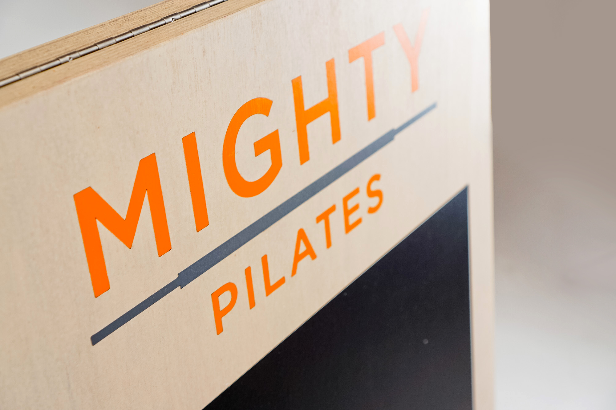 Light wood A-frame sign with orange logo and chalkboard area for class menu for Mighty Pilates, a fitness chain. Light wood A-frame sign with orange logo and chalkboard area for class menu for Mighty Pilates, a fitness chain.