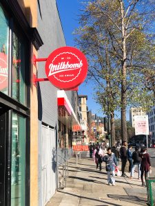 Red circular blade sign with white script for Milkbomb, a sweet stop for donut ice cream sandwiches.