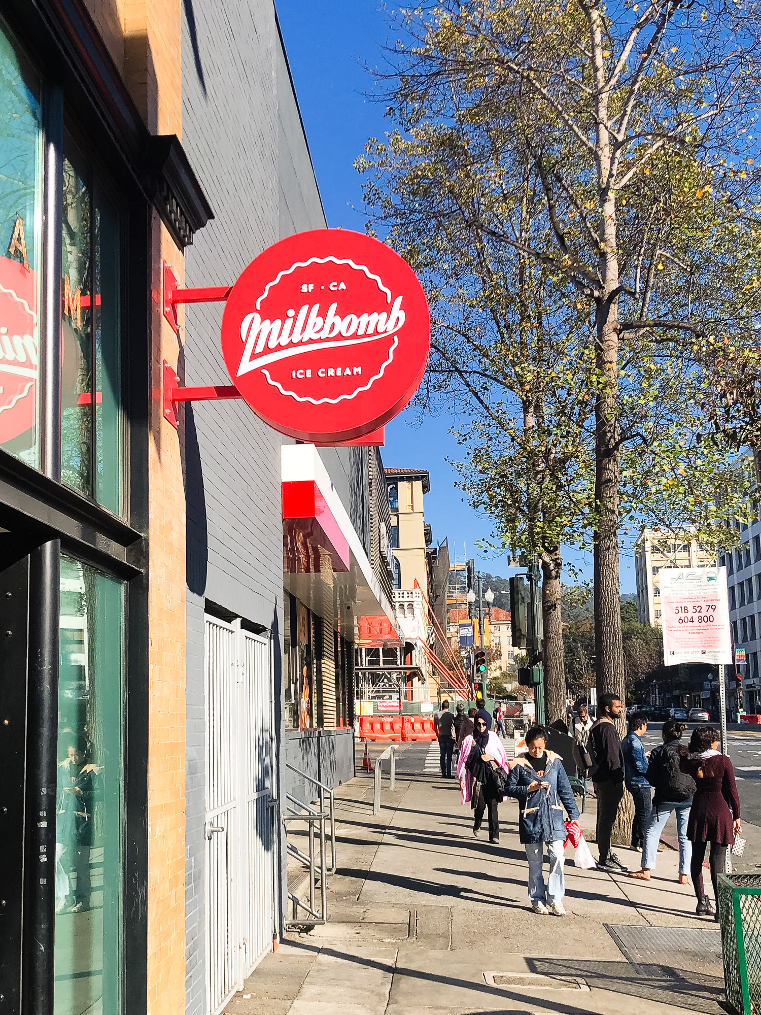 Red circular blade sign with white script for Milkbomb, a sweet stop for donut ice cream sandwiches. Red circular blade sign with white script for Milkbomb, a sweet stop for donut ice cream sandwiches.