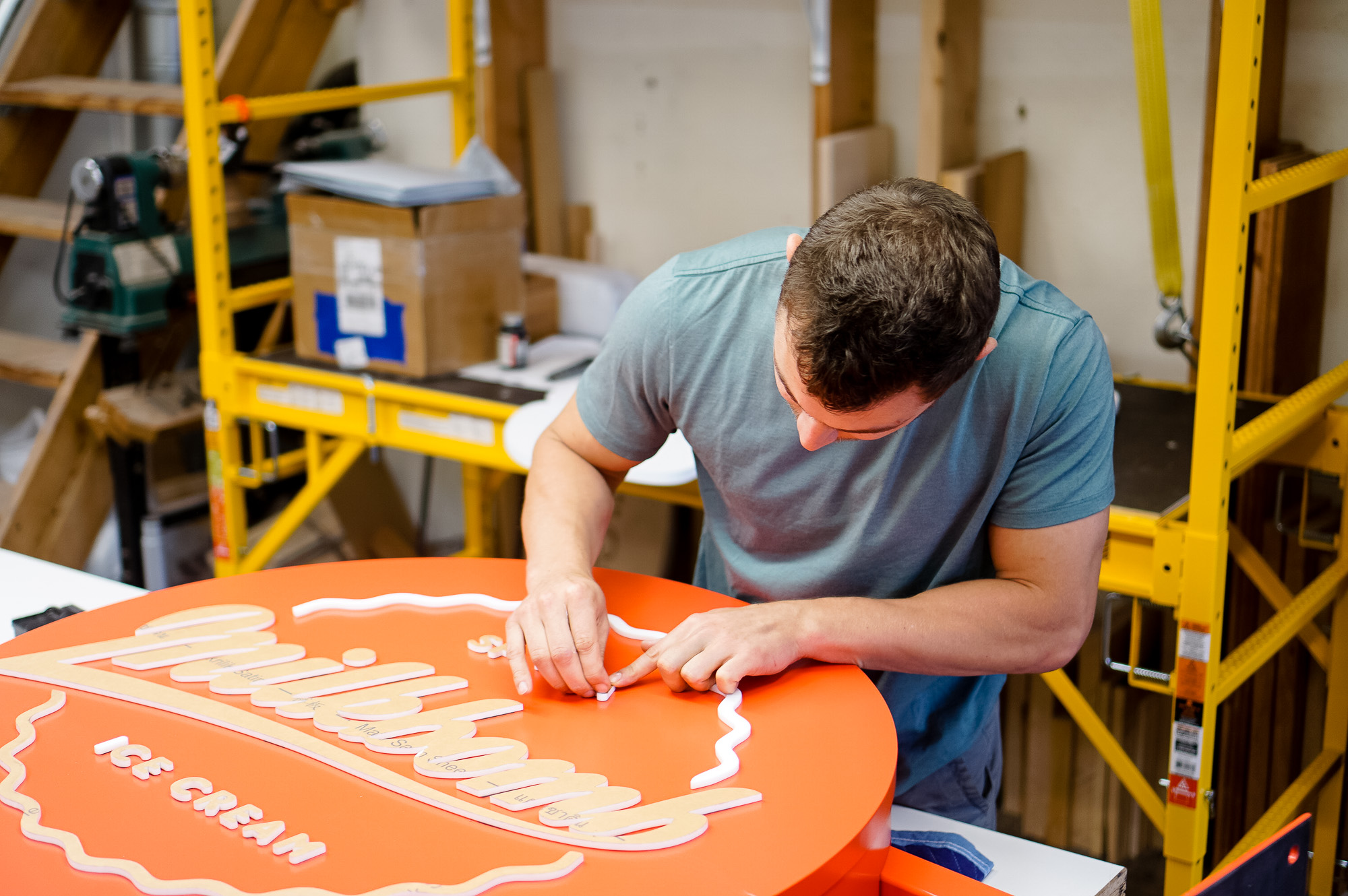 Red circular blade sign with white script for Milkbomb, a sweet stop for donut ice cream sandwiches.