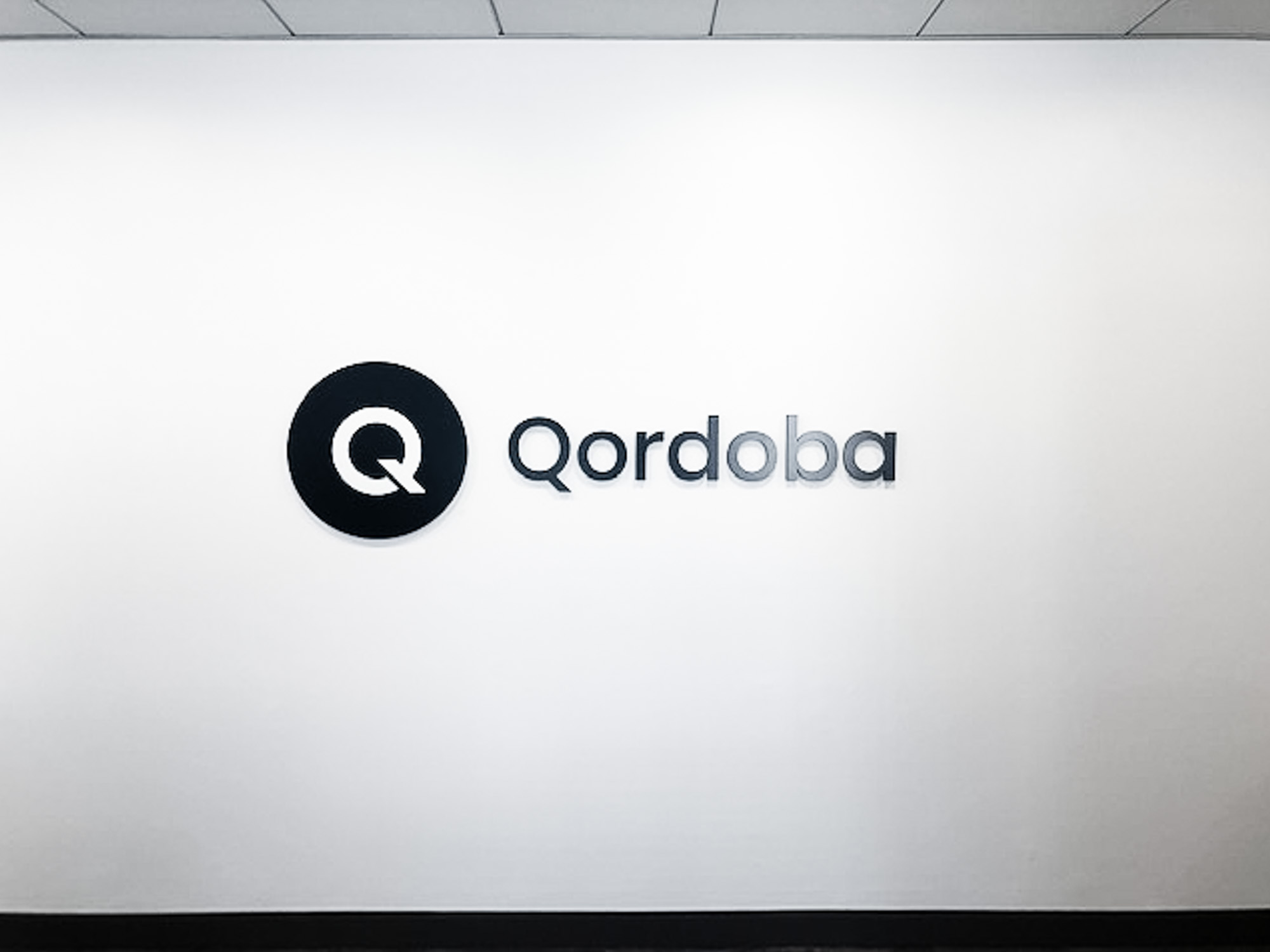 Black and white circular sign on white wall for the office of Qordoba, a content AI technology to help organizations achieve consistency and clarity across all types of content.