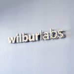 Illuminated, back-lit metal sign on slate colored wall for Wilbur Labs, a San Francisco-based startup studio building a portfolio of companies.