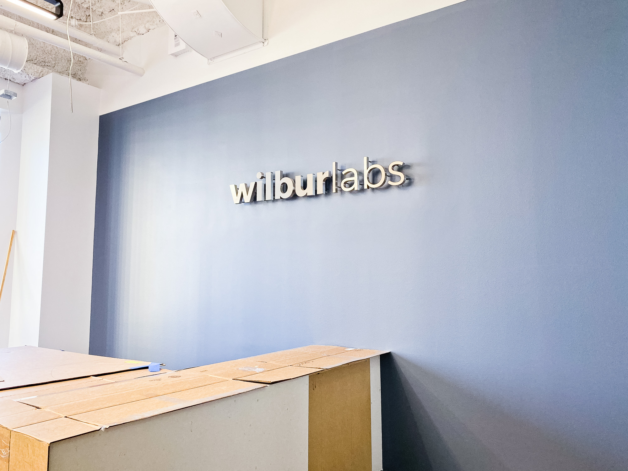 Illuminated, back-lit metal sign on slate colored wall for Wilbur Labs, a San Francisco-based startup studio building a portfolio of companies.