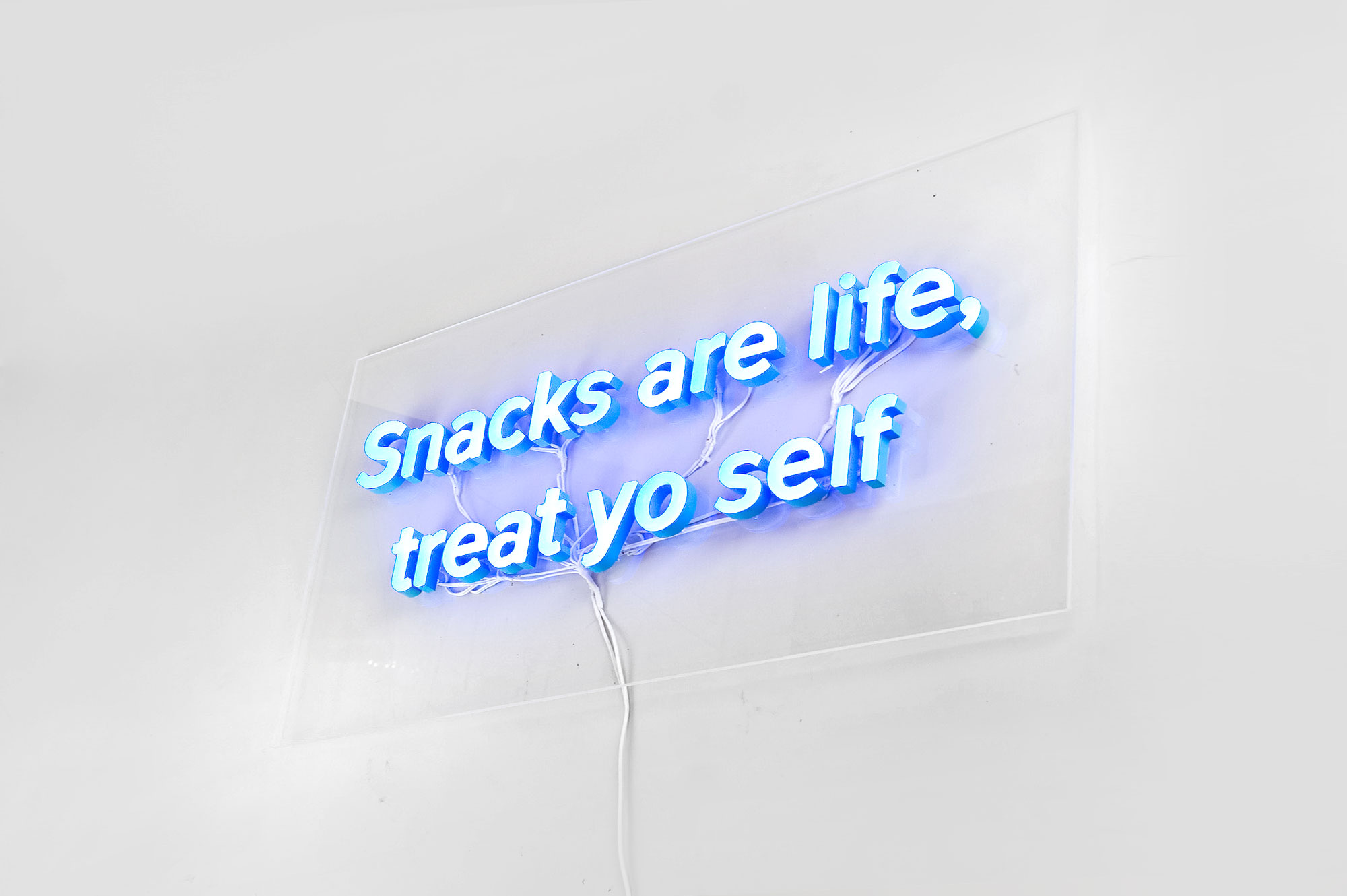 Blue neon style “Snacks are life, treat yo self” sign on clear acrylic backer board with exposed wiring for the kitchen pantry at Zumper, a full-service rental platform. Blue neon style
