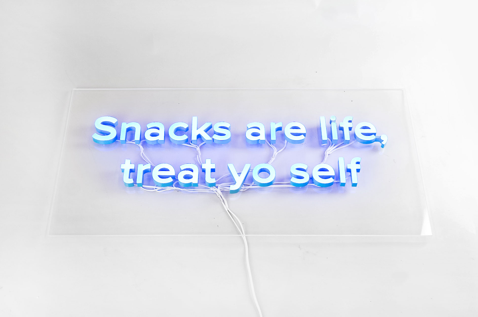Blue neon style “Snacks are life, treat yo self” sign on clear acrylic backer board with exposed wiring for the kitchen pantry at Zumper, a full-service rental platform. Blue neon style