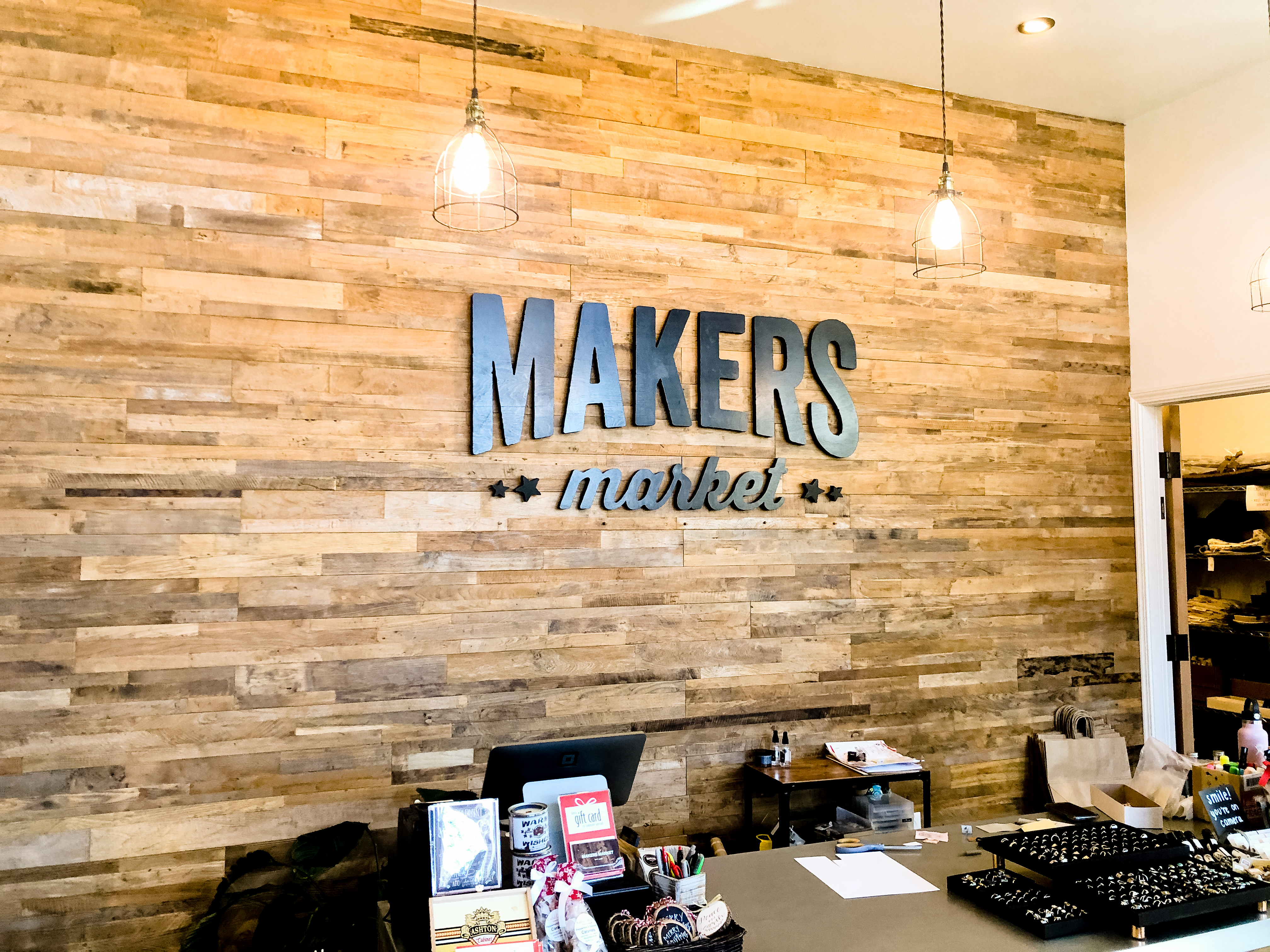 Black distressed wood sign on reclaimed wood wall at the checkout stand / register area for the Napa, CA location of Makers Market, a handcrafted marketplace where you can shop the best of American made goods. Black distressed wood sign on reclaimed wood wall at the checkout stand / register area for the Napa, CA location of Makers Market, a handcrafted marketplace where you can shop the best of American made goods.