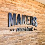 Black distressed wood sign on reclaimed wood wall at the checkout stand / register area for the Napa, CA location of Makers Market, a handcrafted marketplace where you can shop the best of American made goods.