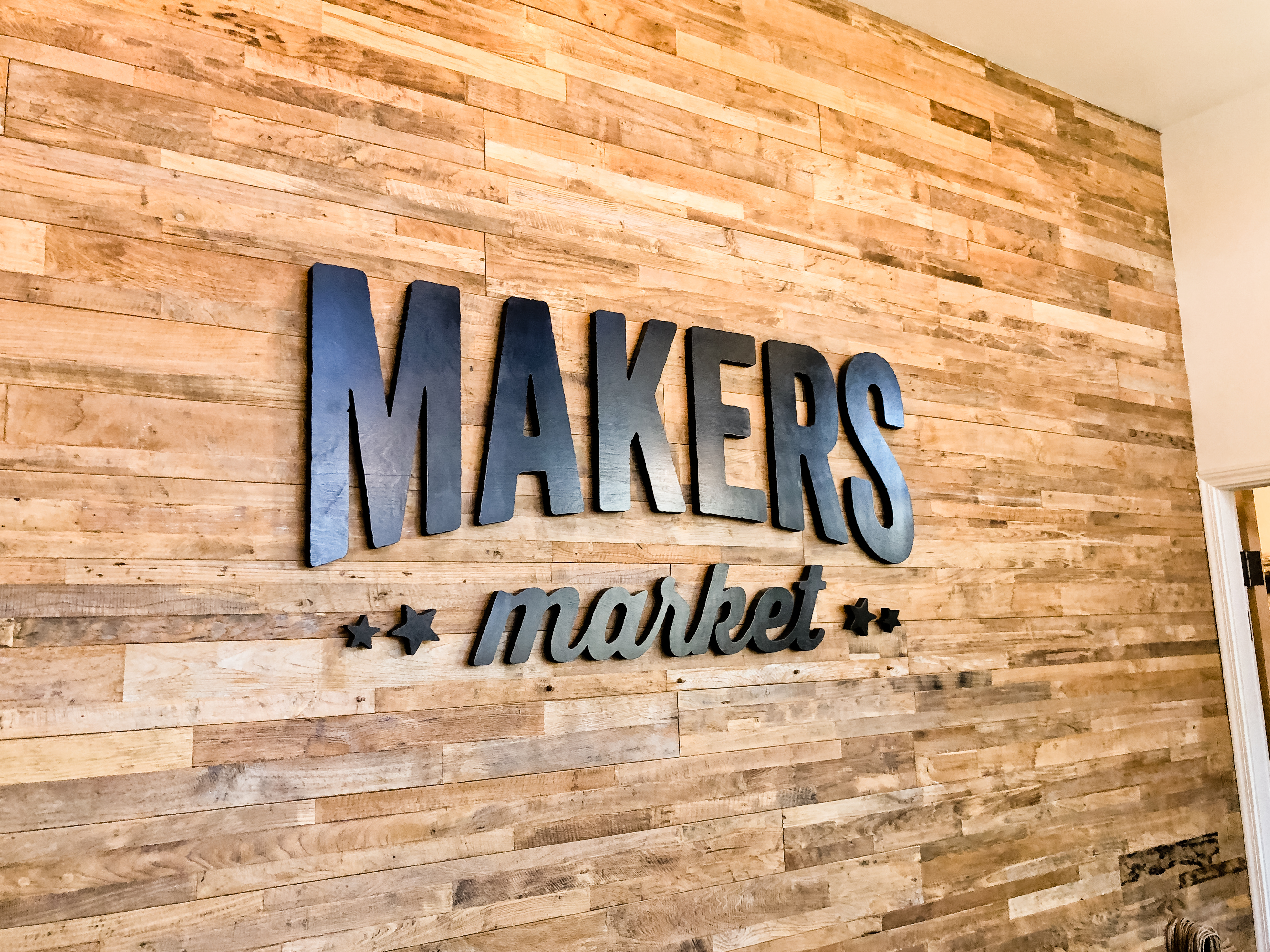 Black distressed wood sign on reclaimed wood wall at the checkout stand / register area for the Napa, CA location of Makers Market, a handcrafted marketplace where you can shop the best of American made goods.