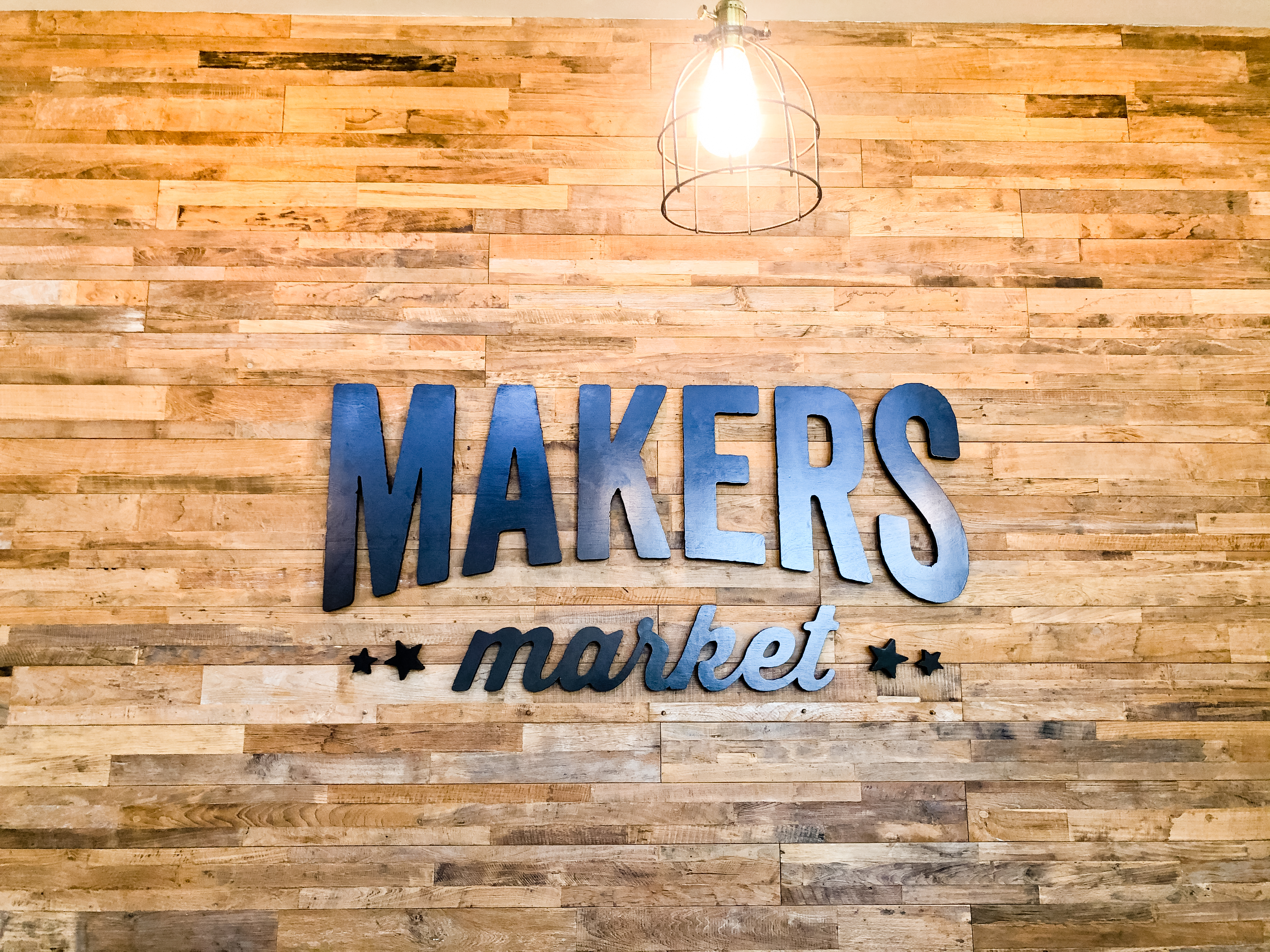 Black distressed wood sign on reclaimed wood wall at the checkout stand / register area for the Napa, CA location of Makers Market, a handcrafted marketplace where you can shop the best of American made goods.