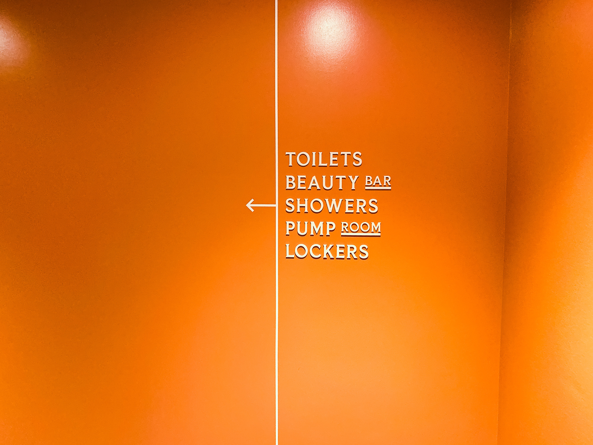 Cream colored, typographic wayfinding sign on orange wall for The Wing, a co-working space in San Francisco.
