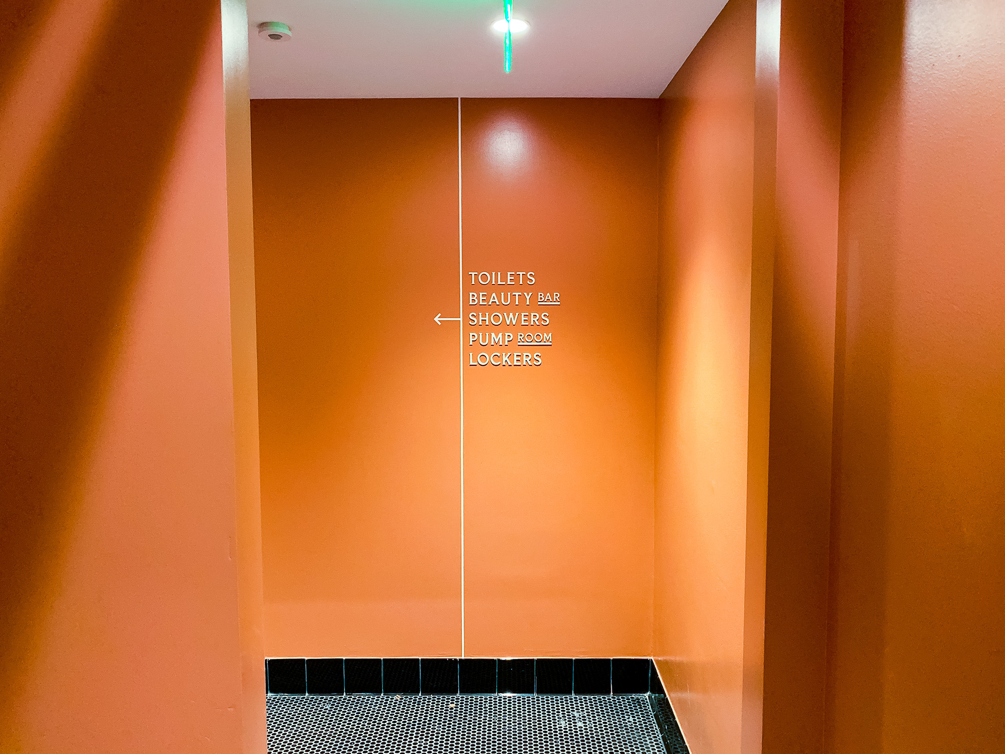 Cream colored, typographic wayfinding sign on orange wall for The Wing, a co-working space in San Francisco. Cream colored, typographic wayfinding sign on orange wall for The Wing, a co-working space in San Francisco.